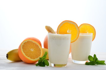 Smoothies with bananas and oranges, a sprig of mint on a white background. Space for text or design.