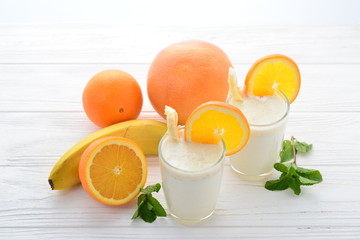 Smoothies with bananas and oranges, a sprig of mint on a white background. Space for text or design.