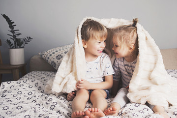 Two pretty kids embrace under blanket
