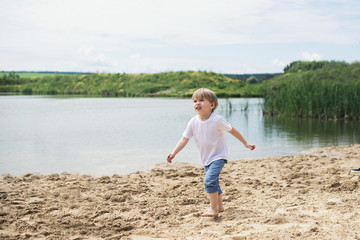 Little boy running on a sand near a pond, summer day