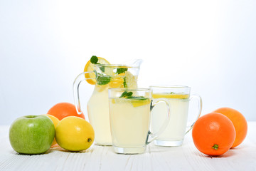 Citrus lemonade water with lemon sliced , healthy and detox water drink in summer on white wooden table with apple, oranges and lemons.