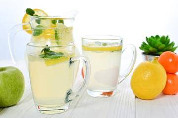 Citrus lemonade water with lemon sliced , healthy and detox water drink in summer on white wooden table with apple, oranges and lemons.