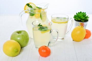 Citrus lemonade water with lemon sliced , healthy and detox water drink in summer on white wooden table with apple, oranges and lemons.