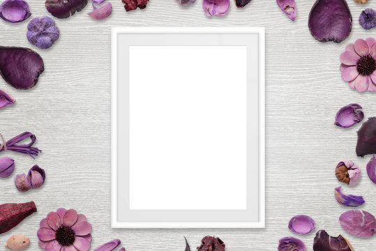 Picture frame with isolated white space for picture or text. Flower decorations around the frame. White wooden desk in background. Top view.