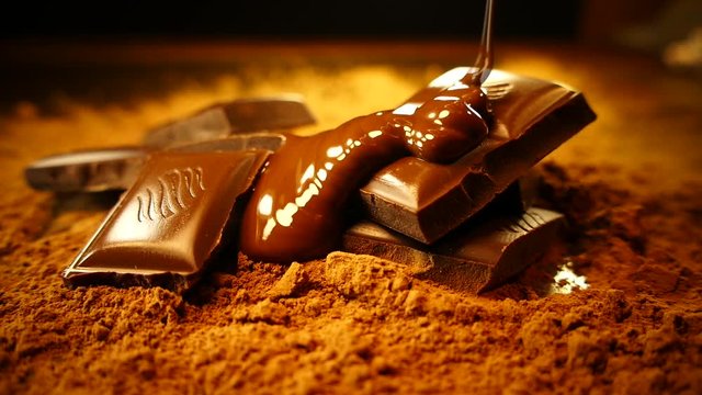 Pieces of dark chocolate are poured with melted chocolate. Liquid chocolate spreads and flows down a wooden board