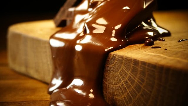 Pieces of dark chocolate are poured with melted chocolate. Liquid chocolate spreads and flows down a wooden board