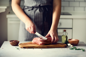 Wooman hands cutting beef meat on wooden chopping board, rosemary, oil, salt, pepper. Girk cooking...
