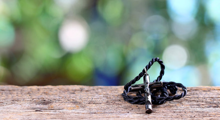 cross necklace on a wood mock up over blurred green garden bokeh light.