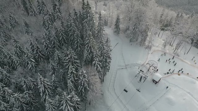 Snow forest and skiers on a ski lift pov. Aerial view. Winter alpine ski resort.