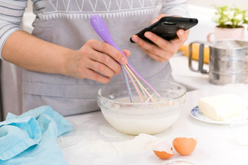 Woman in apron mixing eggs in ceramic bowl for dough on wooden table in the kitchen. Cooking process for step by step recipe.