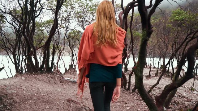 Following young caucasian woman walking towards Kawah Putih White Crater lake between trees