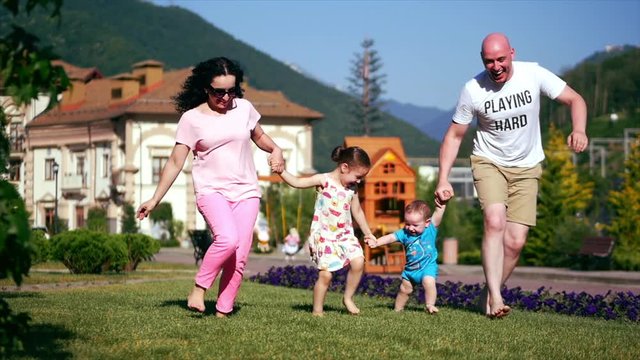Carefree young family happily runs along the green grass holding hands, happy faces of the family.