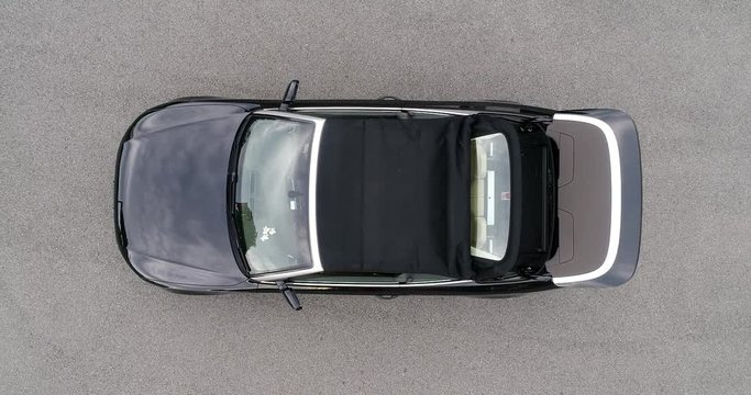 Small sports convertible car unfolding and opening soft top roof and showing young women driver and passenger.
