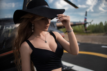 Beautiful business lady in black hat and dress. On the background of a black helicopter.