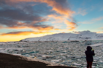 A woman in silhouette is phototraphing Glacier Lagoon (Jokulsarlon) at sunset with her mobile phone on the south coast of Iceland. It contains thousands of icebergs from the Breidamerkurjokull Glacier
