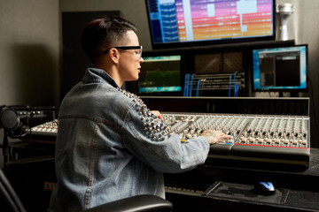 Pensive busy hipster young woman in denim jacket working on professional analog mixing console...