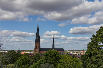 Fototapeta premium Profile of Uppsala Cathedral in Sweden under a blue sky with fluffy white clouds, green trees in the foreground