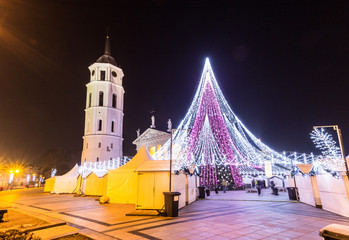 Fototapeta premium VILNIUS, LITHUANIA - DECEMBER 31 2017: night view of the christmas tree on central square, belfry and Cathedral of St. Stanislaus and St. Vladislav on the new years eve.