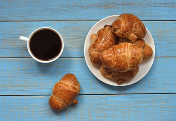 coffee mood. country breakfast background. a cup of black coffee and a plate with freshly baked croissants with golden crust on a blue retro wooden table