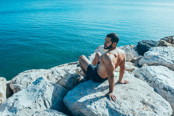 Strong Man Sunbathing and Sitting on Stones at Sea