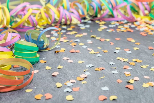 Luftschlangen und Konfetti als Faschingsdekoration auf einer Schieferplatte 