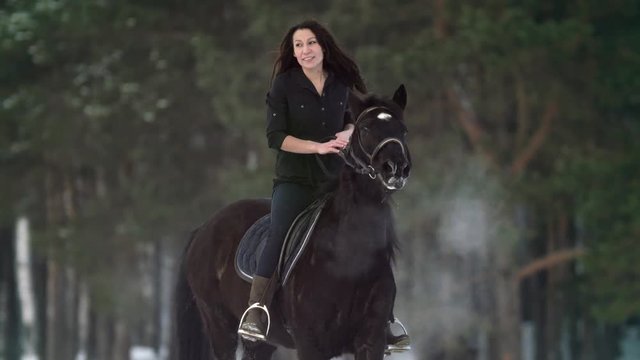 Professional beautiful longhaired woman riding a black horse through the deep snow in the forest, independent stallion prancing, bucking and snorting