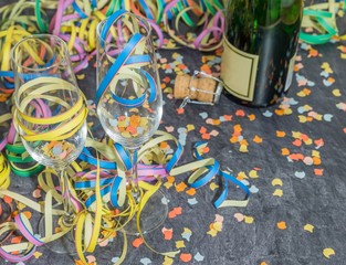Champagner Glas und Flasche mit Faschingsdekoration auf einer Schieferplatte 