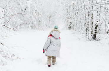 Fototapeta na wymiar Back view of a little girl in a snowsuit walking through a snowy path with deep snow banks on either side.