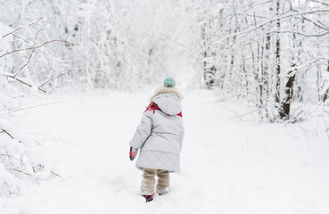 Back view of a little girl in a snowsuit walking through a snowy path with deep snow banks on either side.