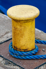 Naklejka premium Gelber Poller mit Roststellen und umgelegtem blauen Tau im Hamburger Hafen bei Tageslicht.