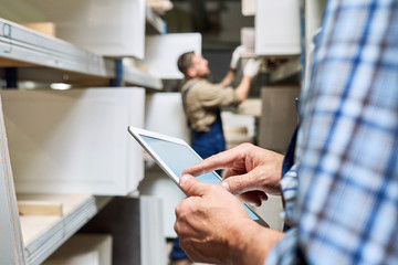 Close up view of unrecognizable worker holding digital tablet while doing inventory in factory storage room, copy space - obrazy, fototapety, plakaty