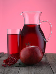 Glass and jar of pomegranate juice with fruit on pink