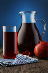 Glass and jar of pomegranate juice with fruit on blue
