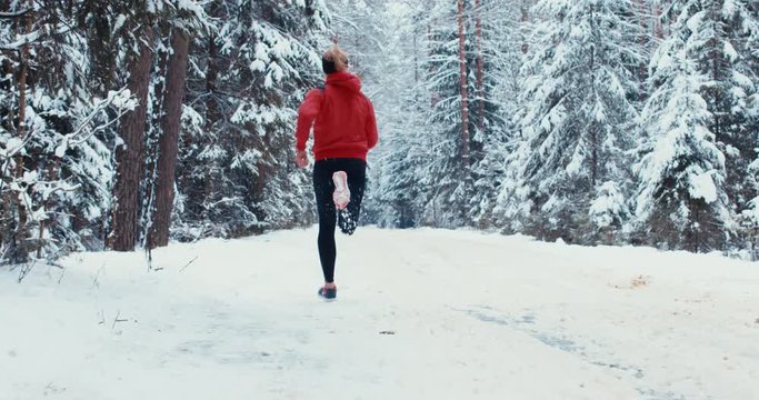 TRACKING Adult fit Caucasian female jogging on beautiful winter forest road. 4K UHD 60 FPS SLO MO