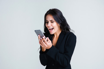 Fototapeta premium Do you hear me? Beautiful young businesswoman using her smartphone and looking irritated while standing against white background