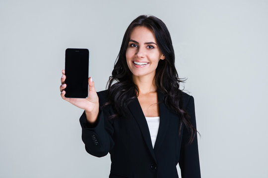 Have you seen this app? Beautiful young businesswoman showing her smartphone and looking at camera with smile while standing against white background