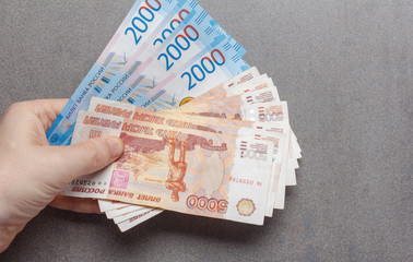 new Russian banknotes denominated in 2000 and 5000 rubles in male hands close-up on a gray...