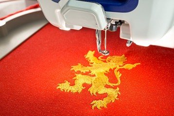 Embroidery machine and  gold lion design on red cotton fabric shirt, close up picture