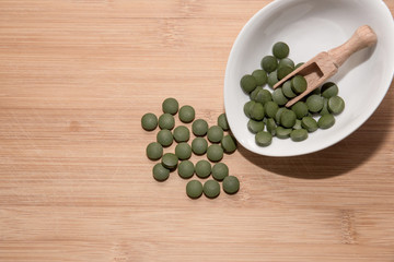 Spirulina,chlorella supplement pills on wooden table. Selective focus