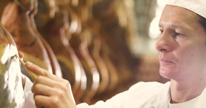 In a ham factory, a man in charge of quality control walks between the hams and controls, the perfume and the certified Italian quality. Concept of: tradition, Italy, food, ham