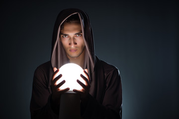 Young wizard with crystal ball in dark room