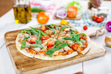 hot fresh homemade traditional italian pizza with cheese, tomatoes and rocked salad on wooden cooking table. wallpaper for pizzeria and food concept. soft focus