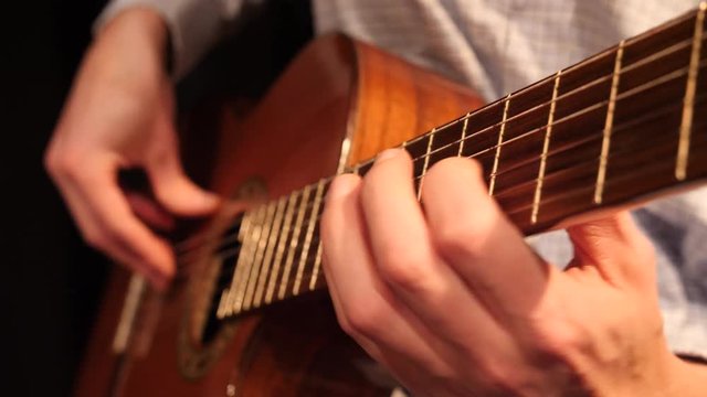 Man playing acoustic guitar, close shot of guitar and hands.