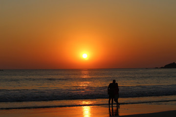 A couple on a beach watching sunset