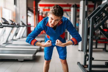 Skinny man in sportswear shows his muscles, gym - obrazy, fototapety, plakaty