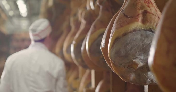 In a ham factory, a man in charge of quality control walks between the hams and controls, the perfume and the certified Italian quality. Concept of: tradition, Italy, food, ham