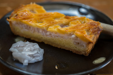 One piece coconut tart large is placed on a black plate. Looks very appetizing, on a wooden table.