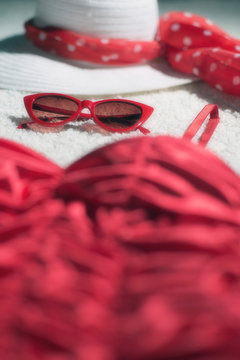 Vintage summer hat, red sunglasses and swimsuit displayed on white carpet floor.