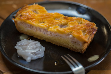 One piece coconut tart large is placed on a black plate. Looks very appetizing, on a wooden table.
