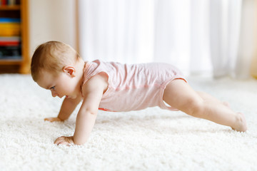 Little funny baby girl lifting body and learning to crawl.